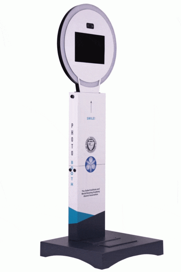 A standalone photo booth with a circular light source, a screen for preview, and a camera at the top. The front panel has instructional text and branding.