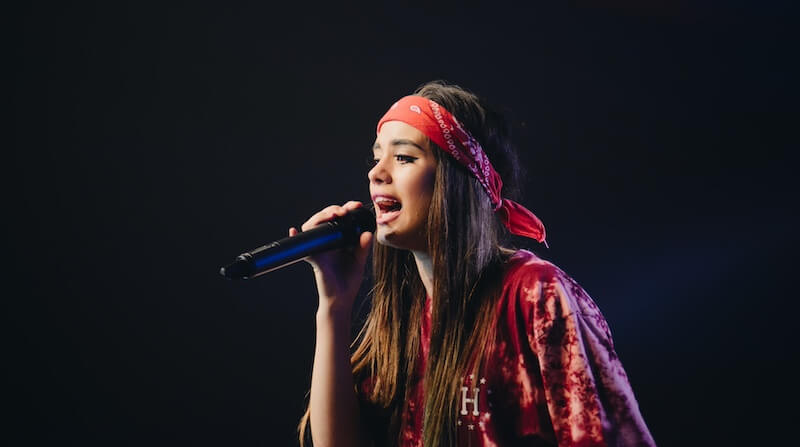 karaoke night party entertainment Person in a red bandana and red shirt sings into a microphone against a dark background.